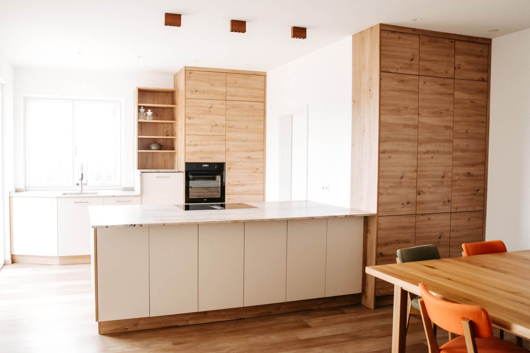 Moderne Küche mit hellem Holz und weißen Schränken, Kochinsel und Esstisch.