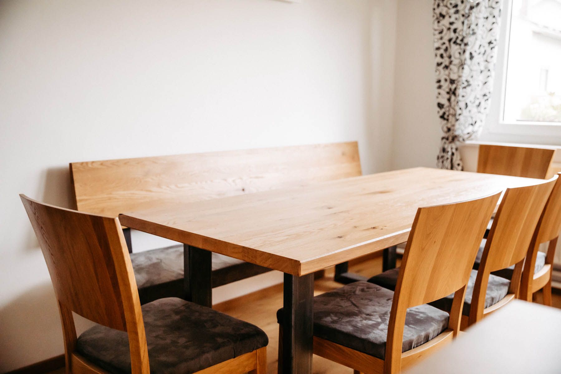 Esstisch aus Holz mit Bank und Stühlen in einem Raum mit natürlichem Licht.