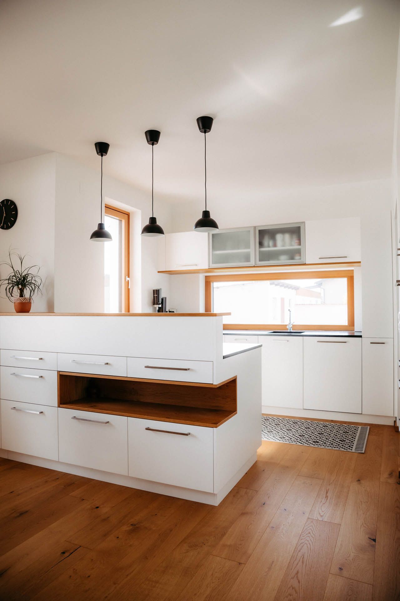 Moderne weiße Küche mit Holzakzenten, Kochinsel und drei Pendelleuchten.