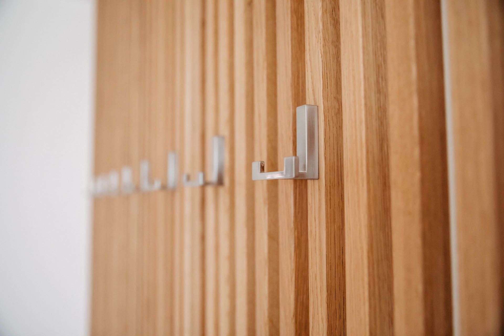 Holzwand mit senkrechten Latten, daran sind Metallhaken befestigt.