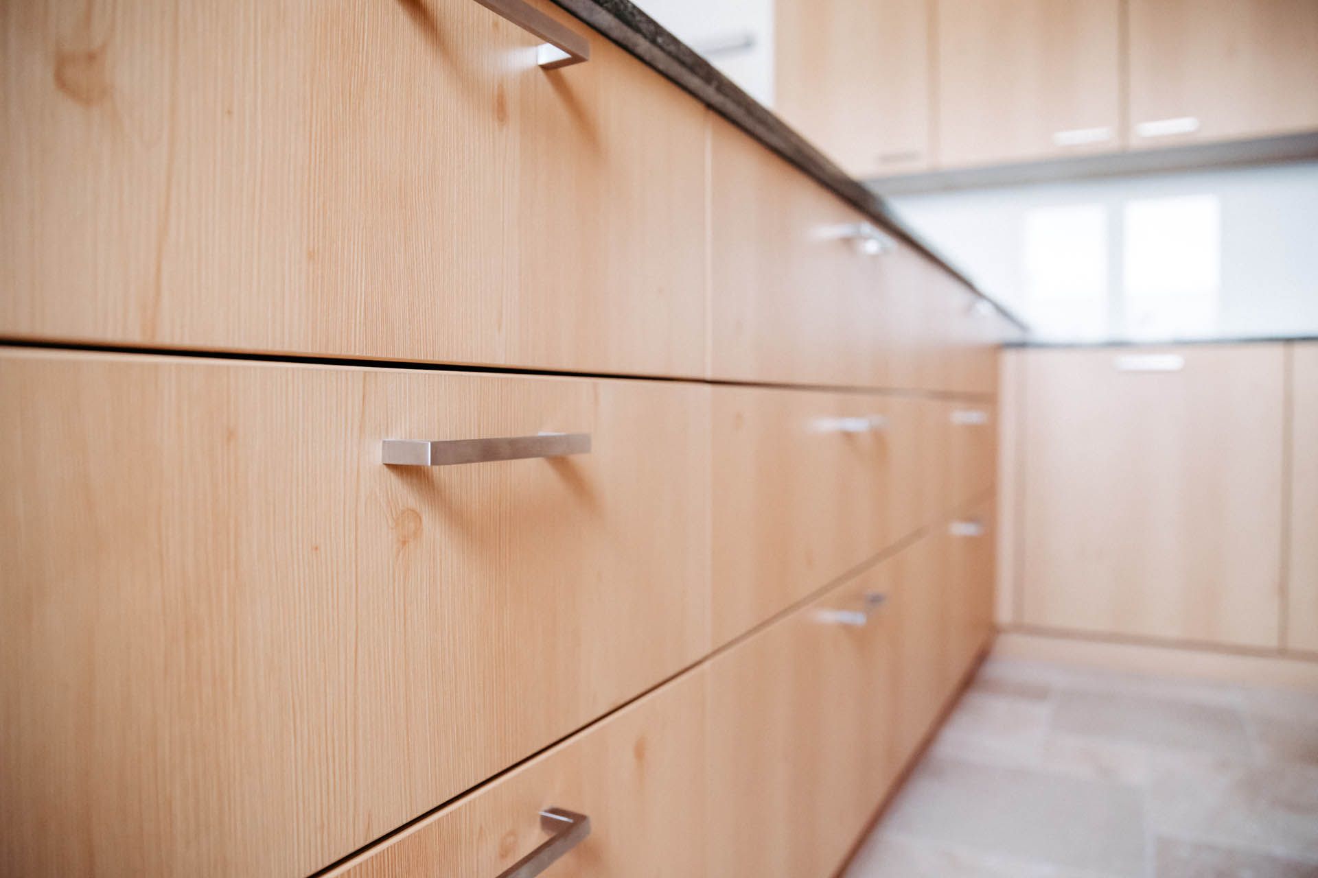 Küchenschränke aus hellem Holz mit silbernen Griffen, Schrägansicht.
