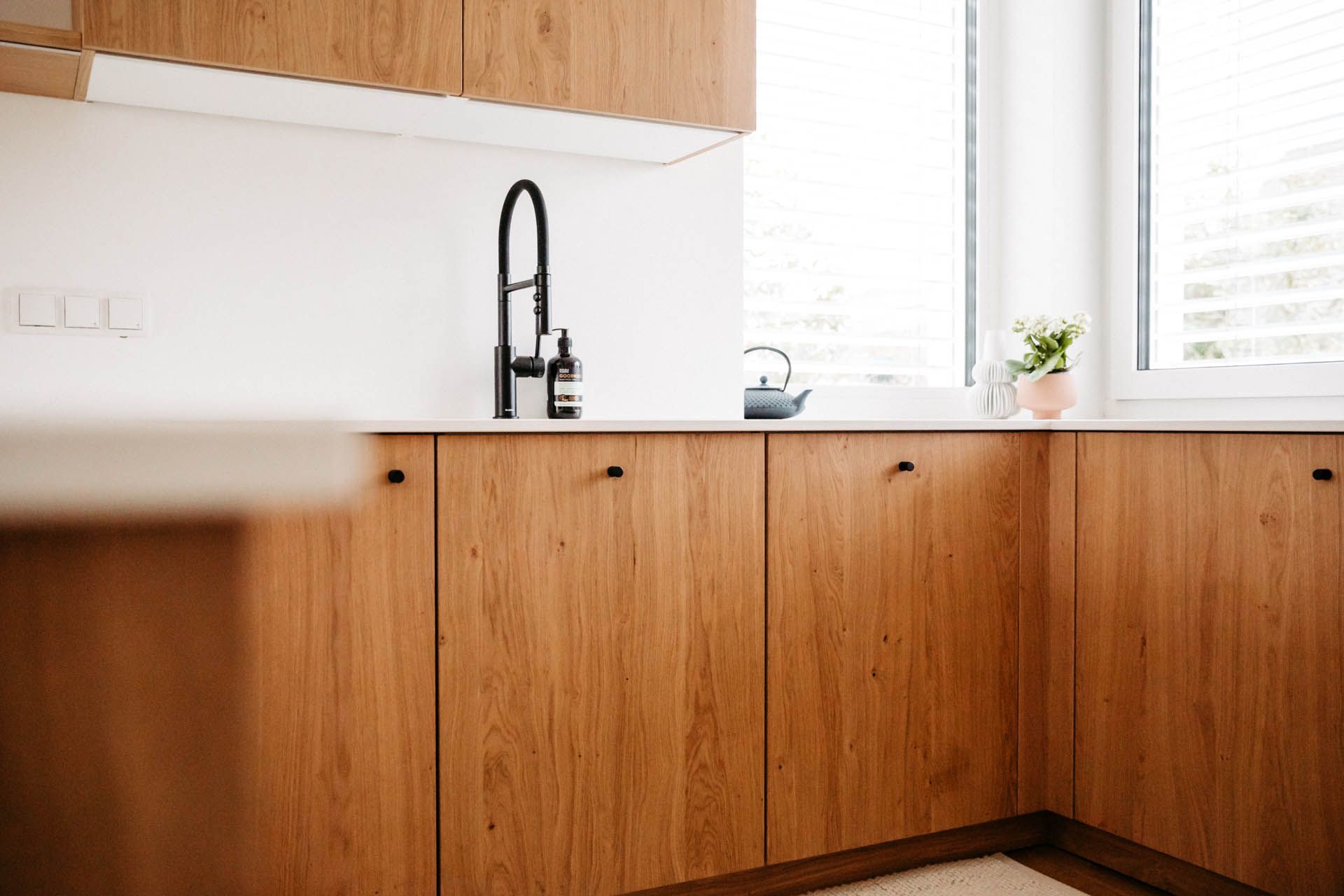 Küchenschränke und Arbeitsplatte aus Holz mit schwarzem Wasserhahn und einem Fenster.