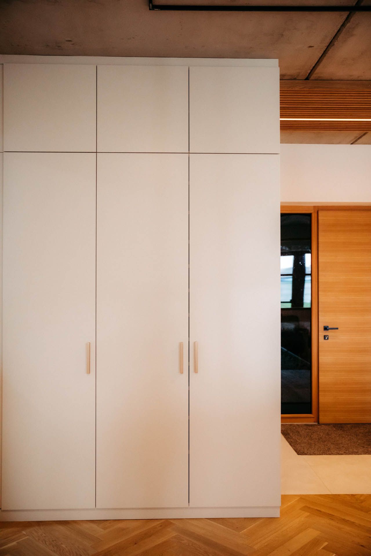 Weißer Schrank mit Holzgriffen neben einem Türrahmen und einer Holztür, Fischgrätboden.