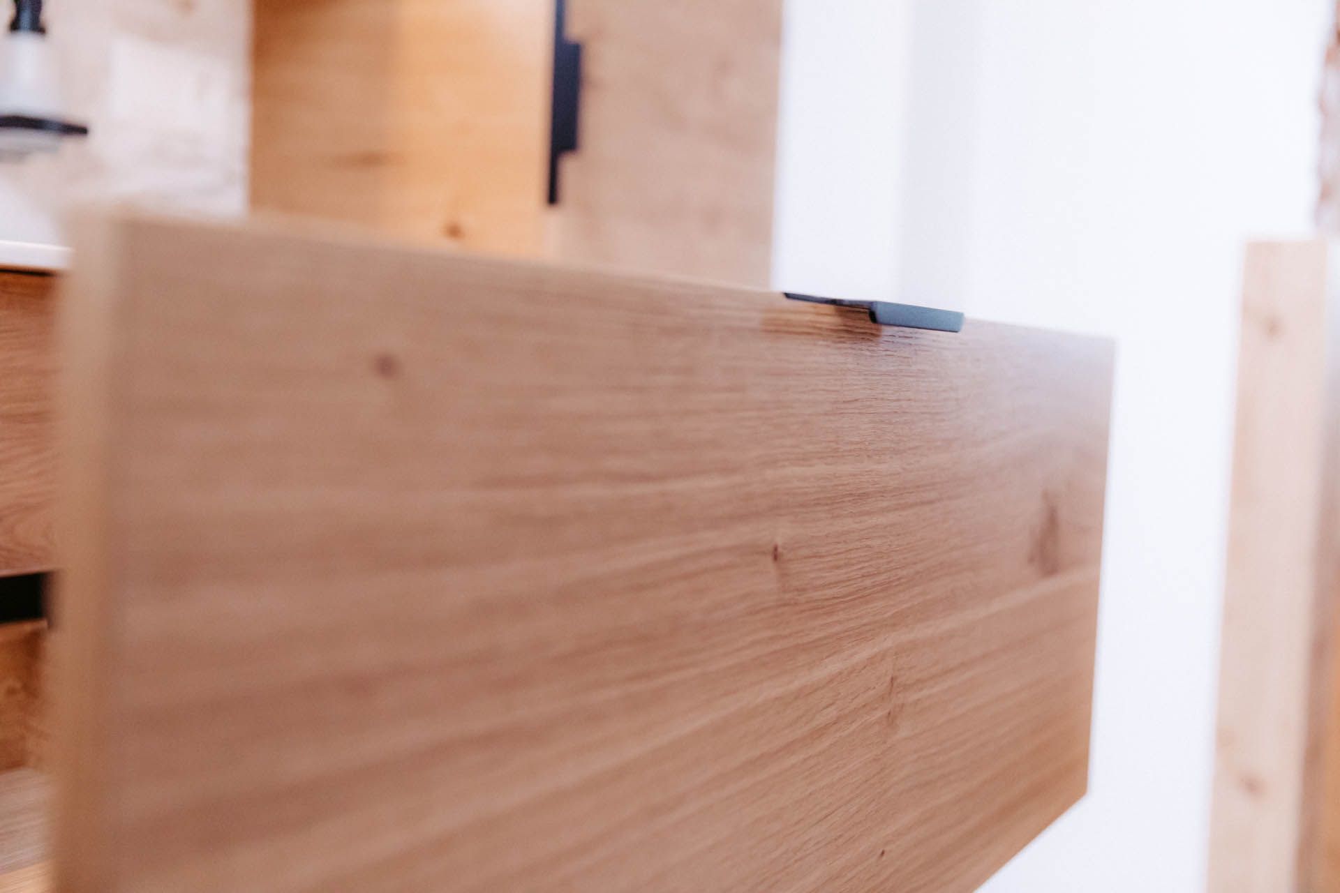 Nahaufnahme eines Holzbretts mit dunklem Metallgriff, das an einer hellen Wand befestigt ist, möglicherweise einem Regal.