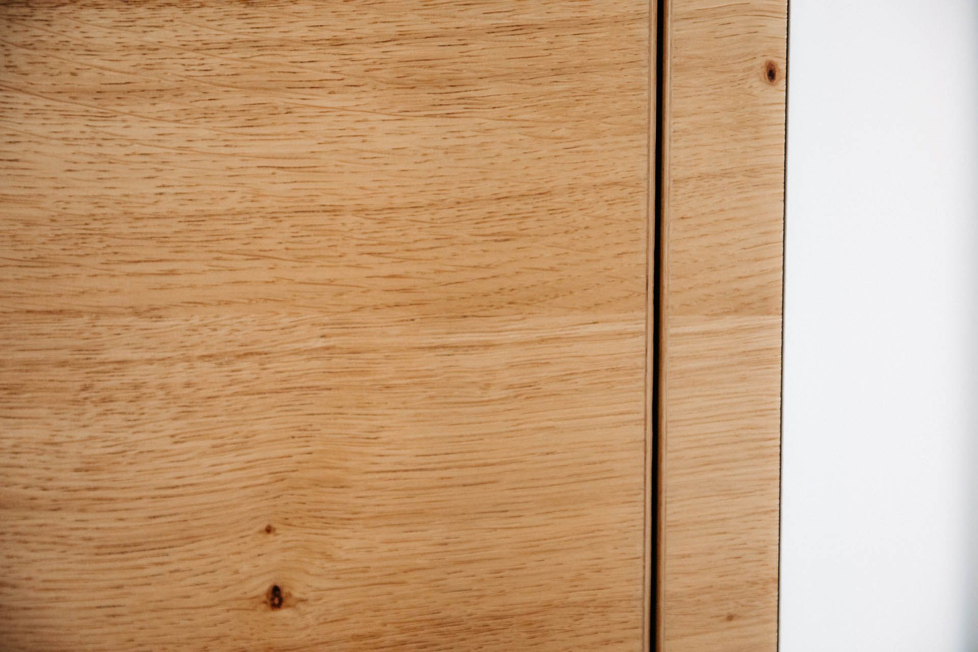 Nahaufnahme einer Holzpaneele, hellbraune Maserung, mit einer dünnen dunklen Naht und einer weißen Wandkante.