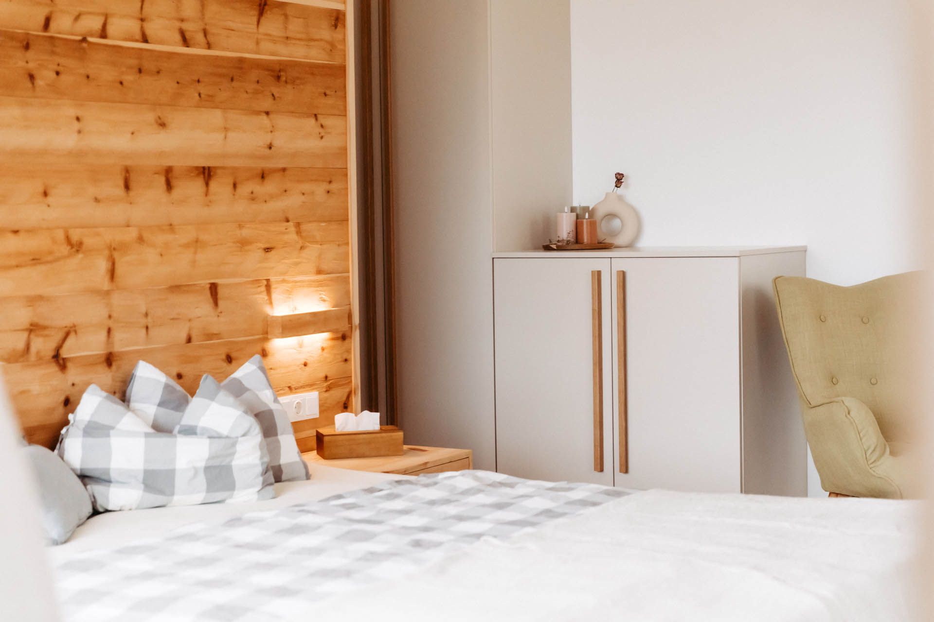 Schlafzimmer mit Holzkopfteil, grauer Bettwäsche und weißem Schrank.