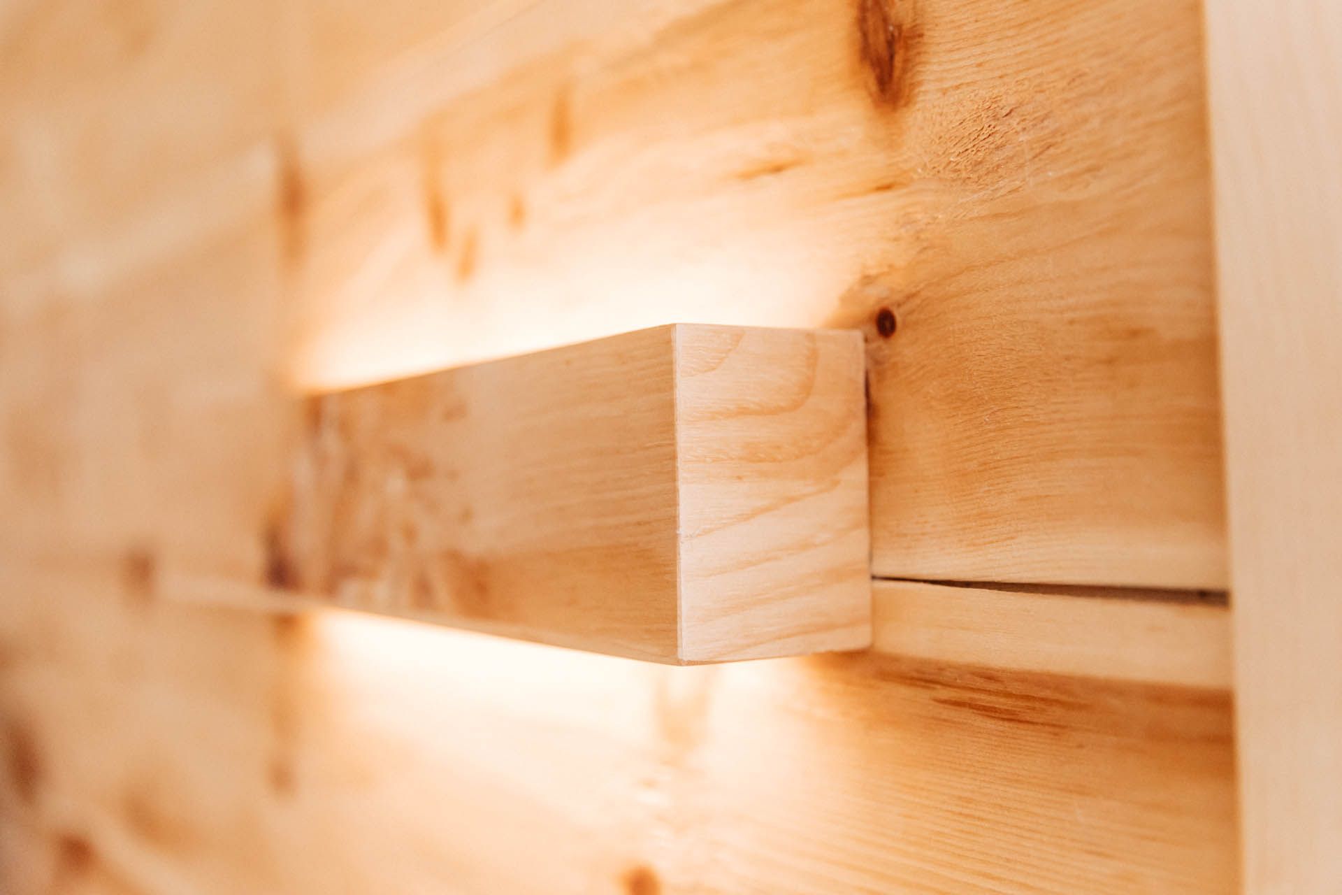 Holzwand mit einem Lichtblock, der aus ihr herausragt und ein warmes Leuchten erzeugt.
