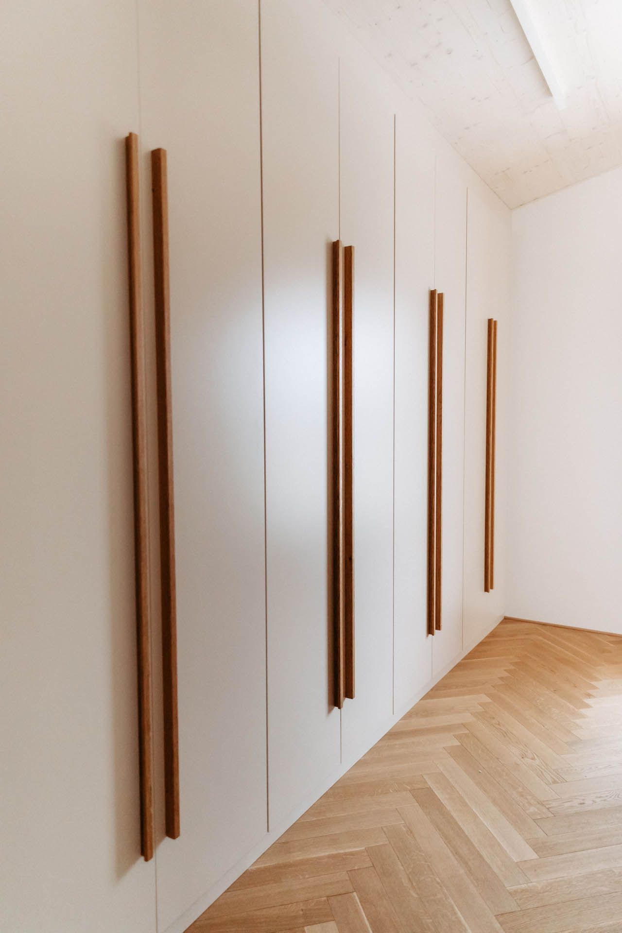 Weiße Schranktüren mit vertikalen Holzgriffen in einem Raum mit Holzböden.