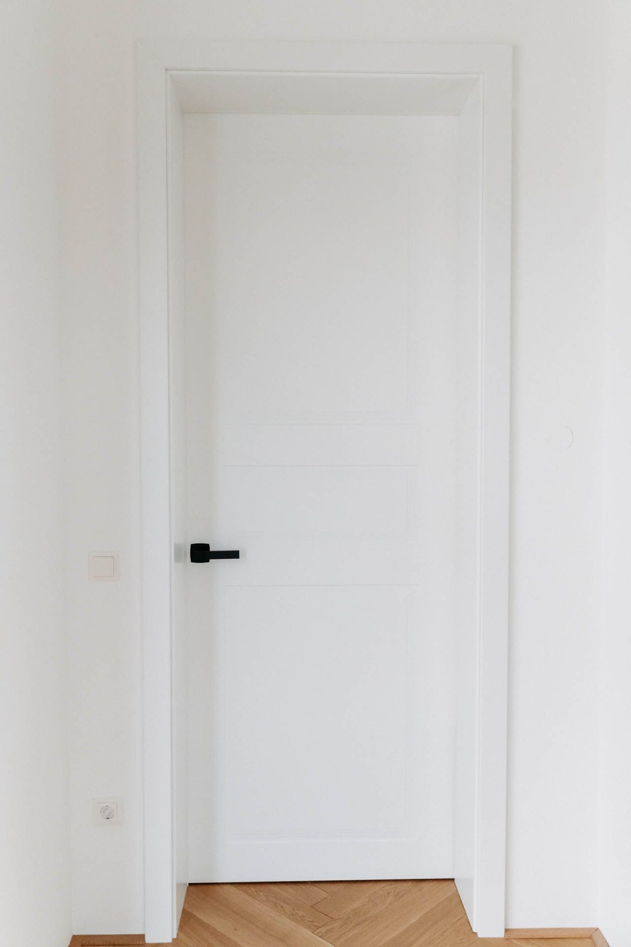 Weiße Tür mit schwarzem Griff, in einem weißen Türrahmen auf einem Holzboden.