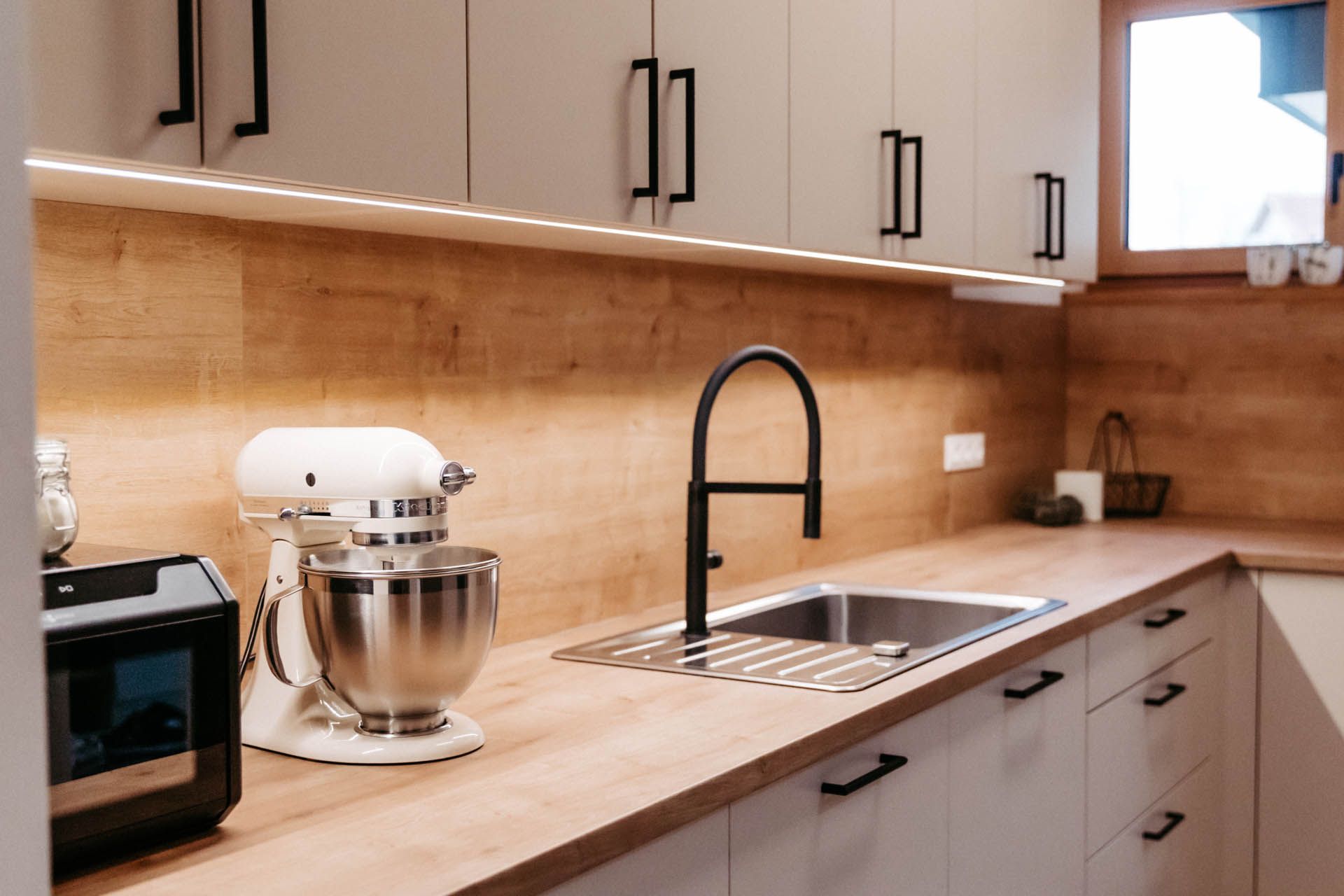 Küche mit hellen Schränken, Holzarbeitsplatten, Spüle und Mixer.