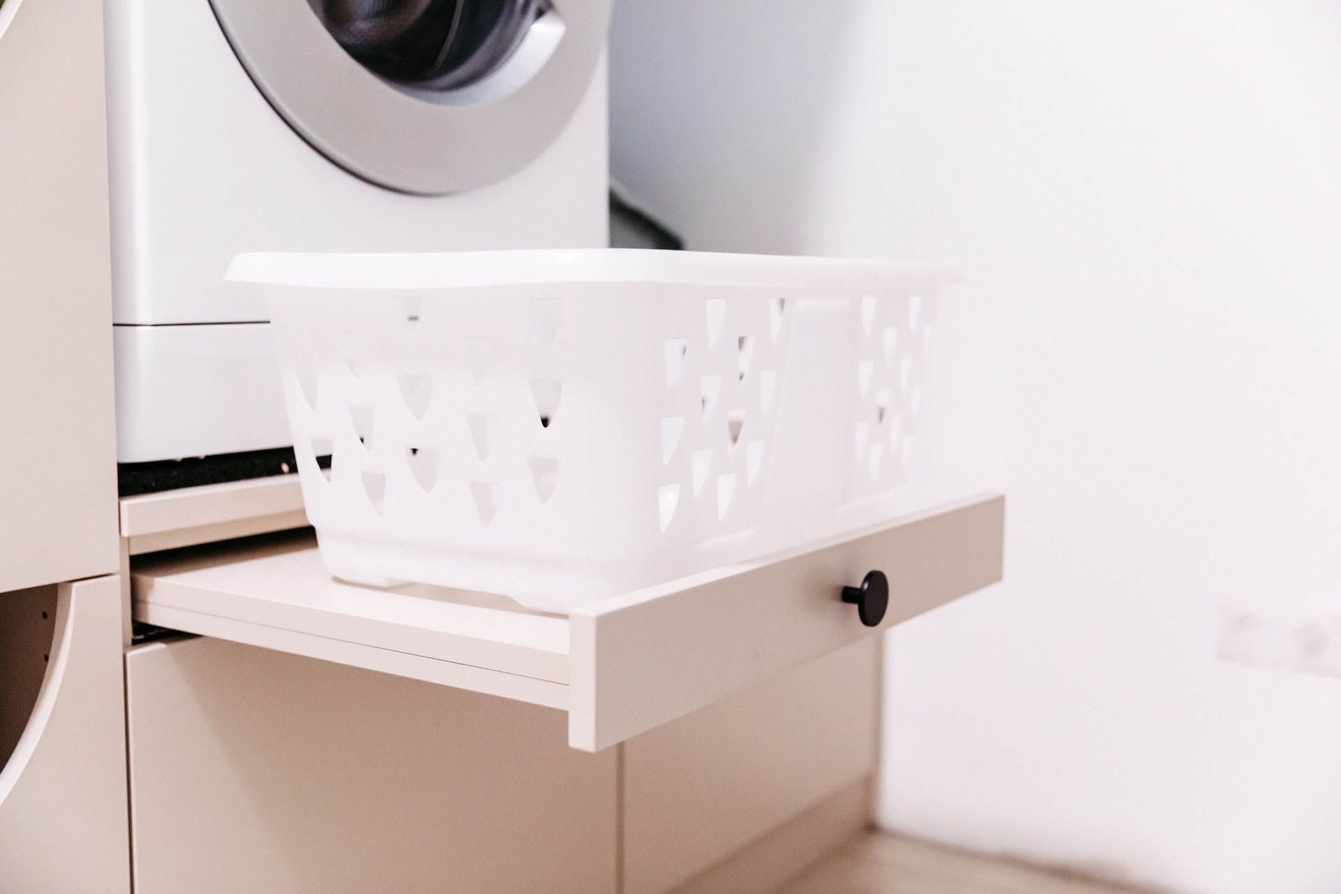 Weißer Wäschekorb auf einem Ausziehregal unter einer Waschmaschine.