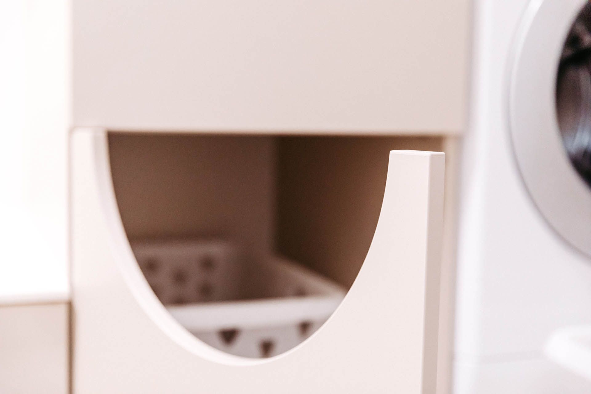 Offener Wäschekorb in einem weißen Schrank, rechts davon eine Waschmaschine.