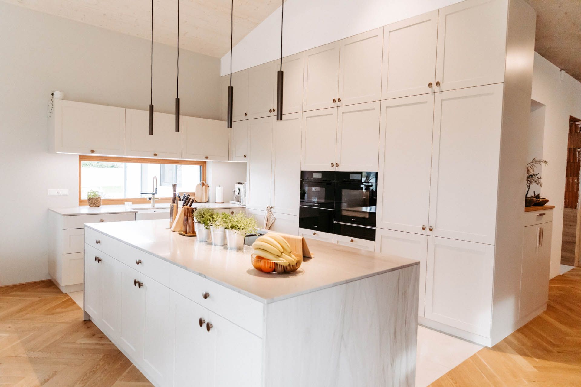 Weiße moderne Küche mit Kochinsel, Schränken und Fischgrätboden.