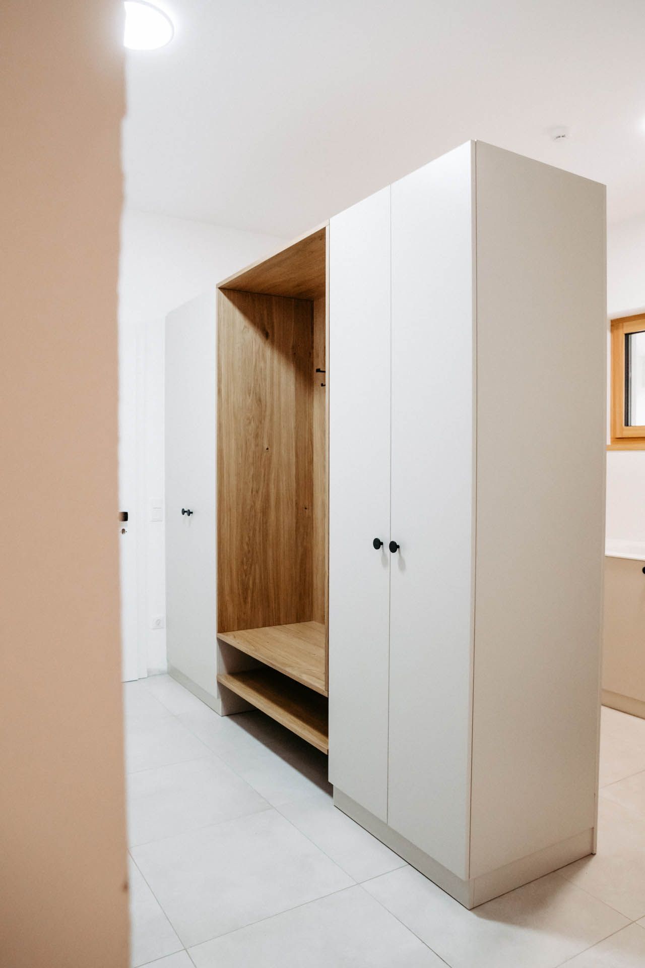 Eingebauter moderner Eingangsschrank mit Holzinnenraum und weißen Außentüren in einem Raum.