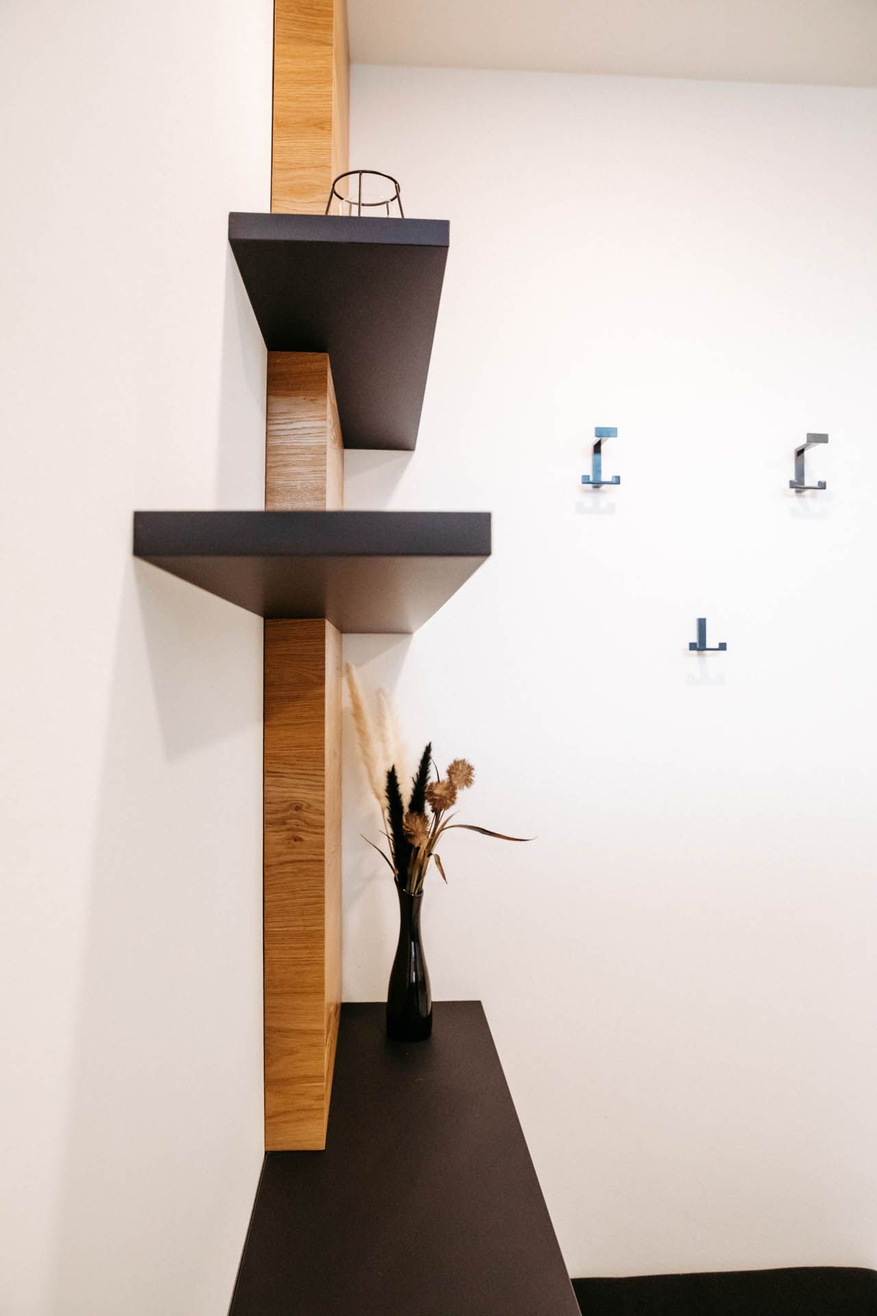 Modernes, minimalistisches Regal mit schwarzen Regalböden und einer strukturierten Holzstütze vor einer weißen Wand, mit dekorativer Vase.