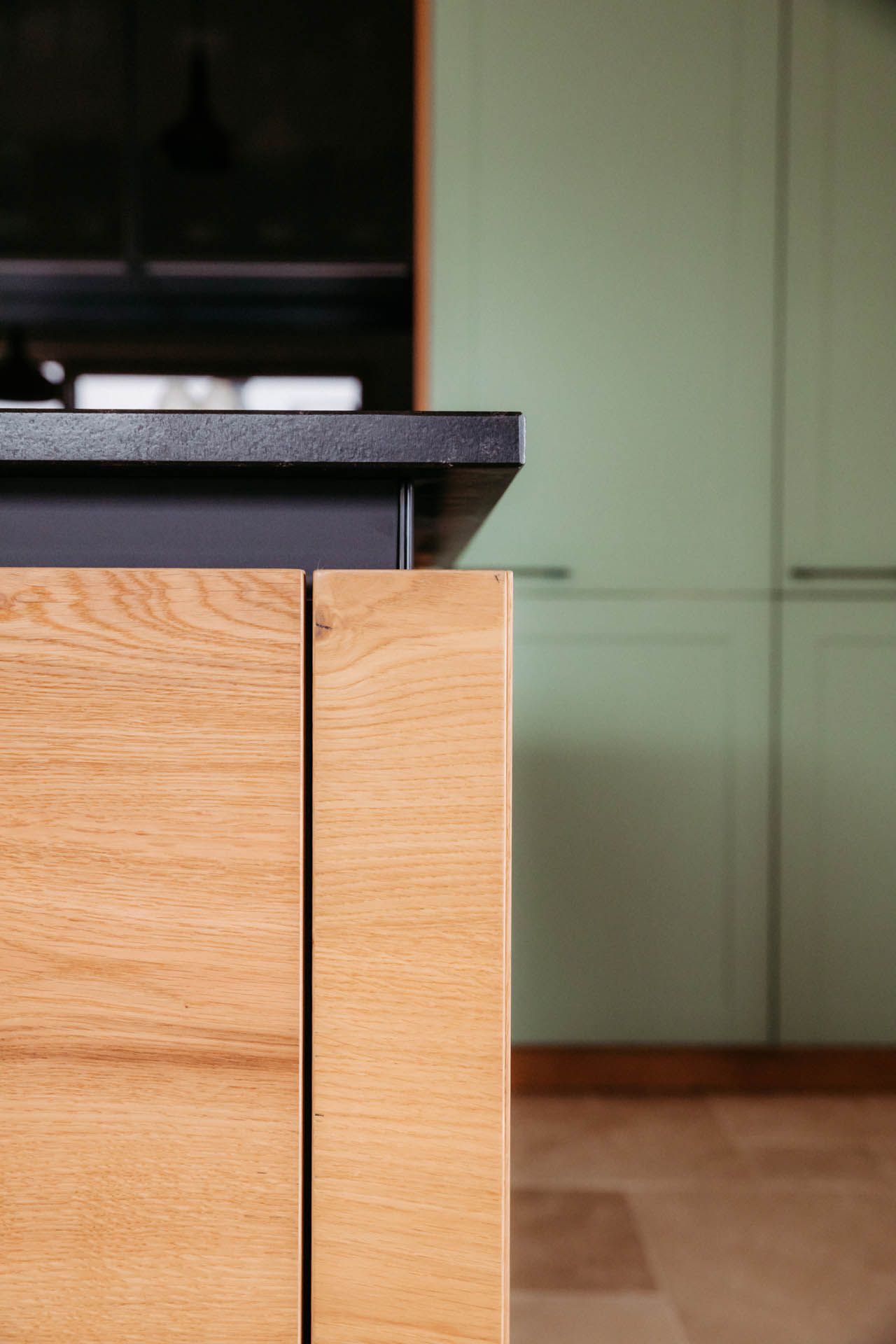 Küchenschrank aus Holz mit dunkler Arbeitsplatte, hellgrüner Schrank im Hintergrund.