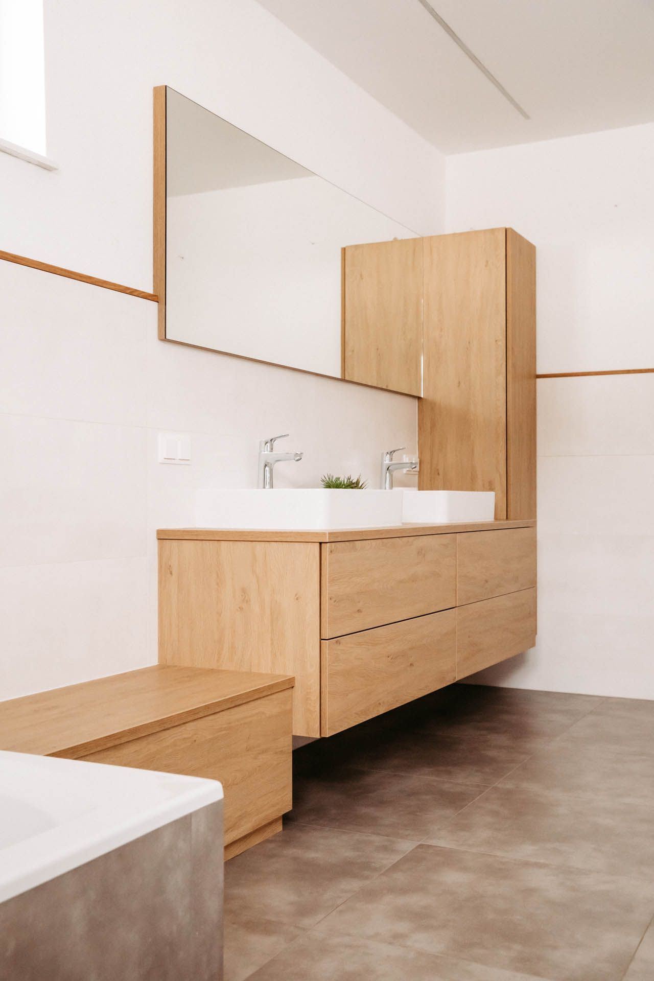 Modernes Badezimmer mit Holzwaschtisch, Doppelwaschbecken, großem Spiegel und einem Schrank vor einer weißen Wand und grauem Boden.