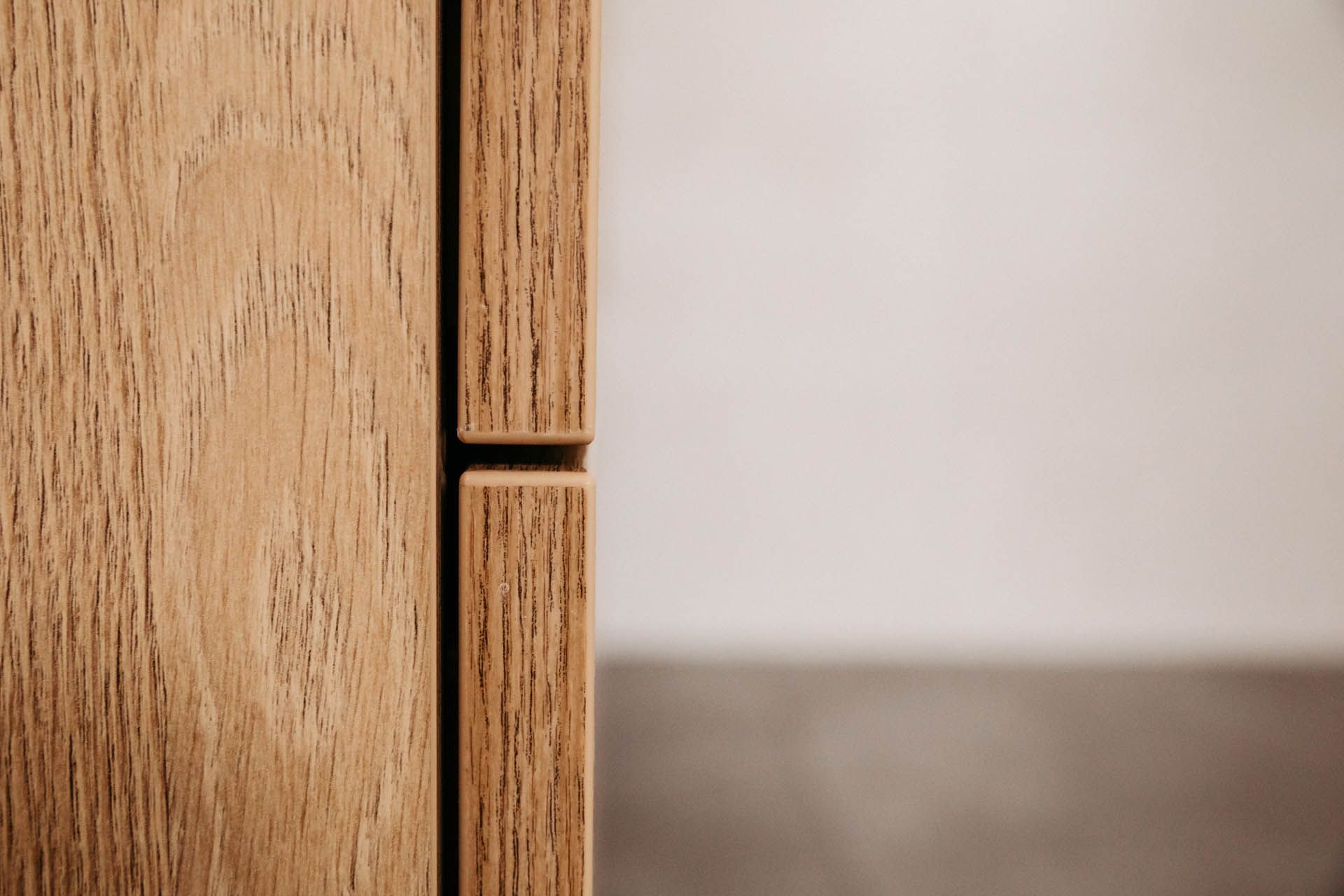 Nahaufnahme der Holztürverbindung eines Schranks, die Maserung und kleine Lücke zeigt; unscharfer neutraler Hintergrund.