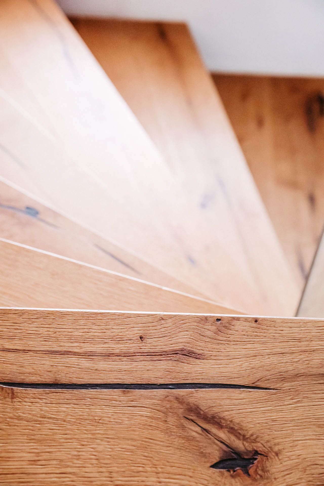 Hölzerne Wendeltreppe, helle Holzmaserung. Nahaufnahme der Stufen.