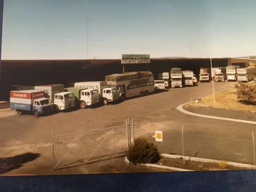 Line of White Trucks and Buses Parked on A Lot Beside a Road Under a Clear Sky — Dawson's Removals In Kelso, NSW