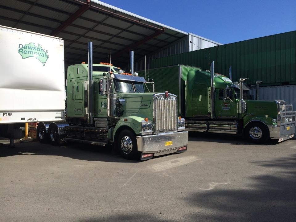Two Green Semi Trucks Parked Outside a Warehouse Loading Dock — Dawson's Removals In Kelso, NSW