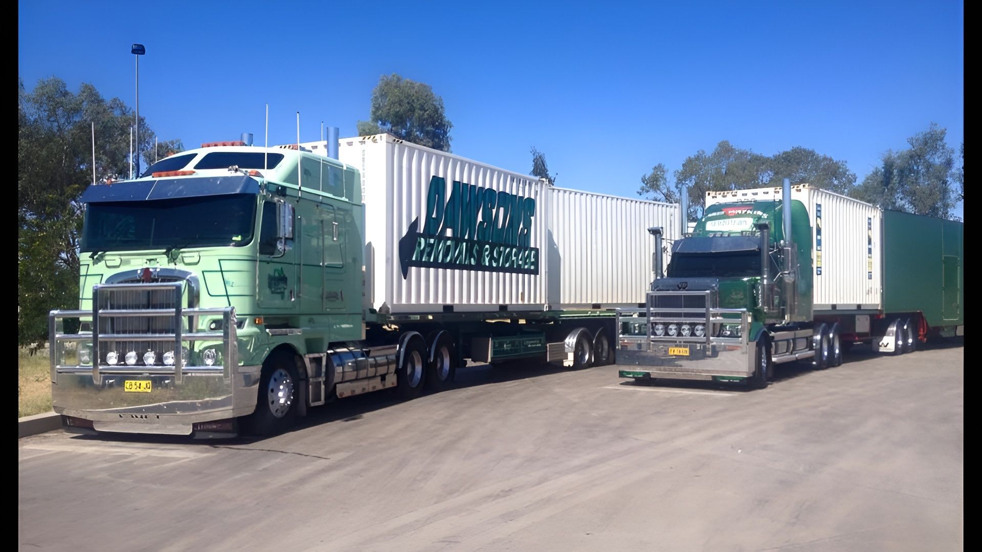 Two Green Semi Trucks Hauling White Trailers Parked on A Sunny Road — Dawson's Removals In Kelso, NSW