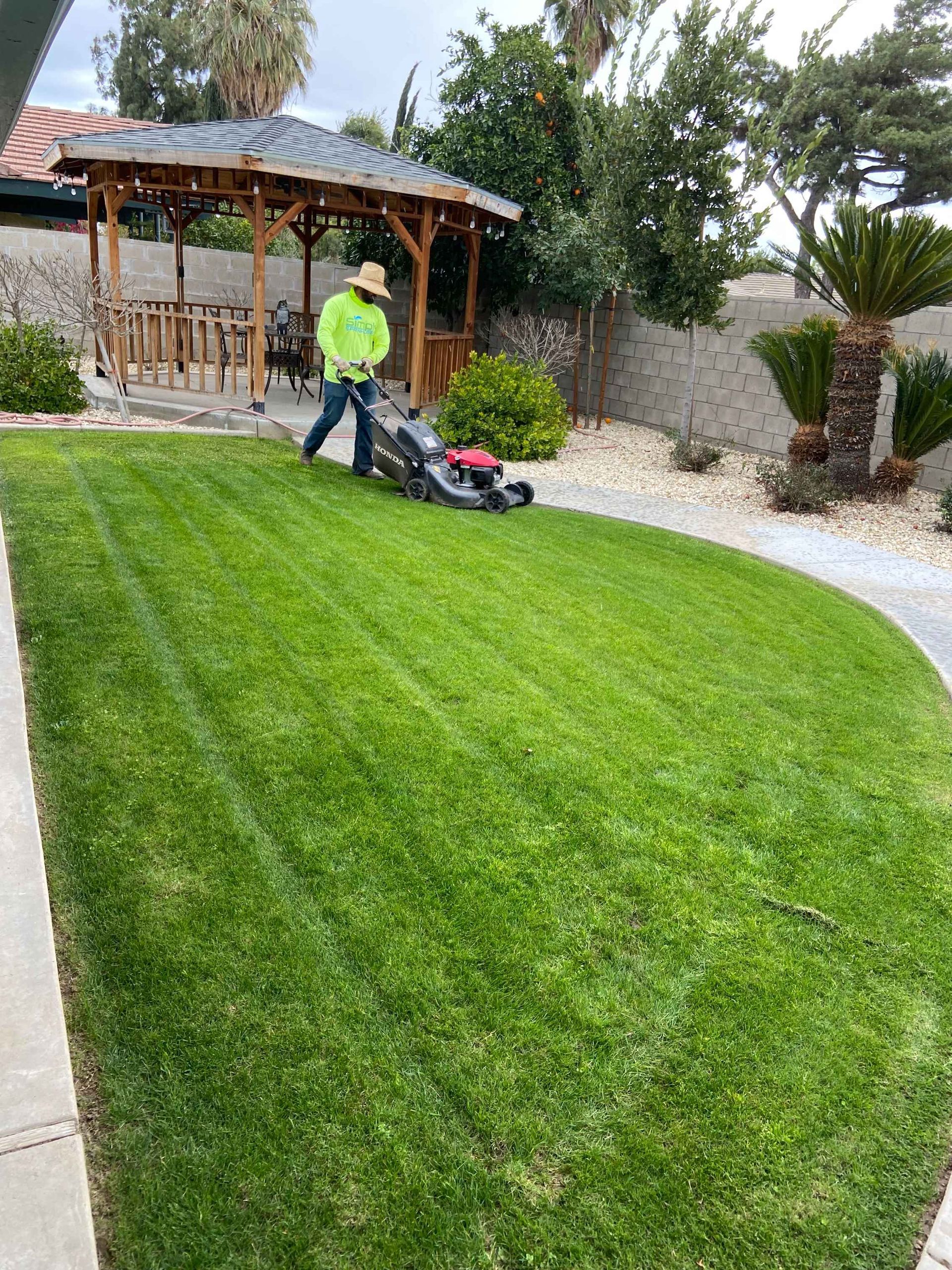 Person mowing lawn in backyard with gazebo.