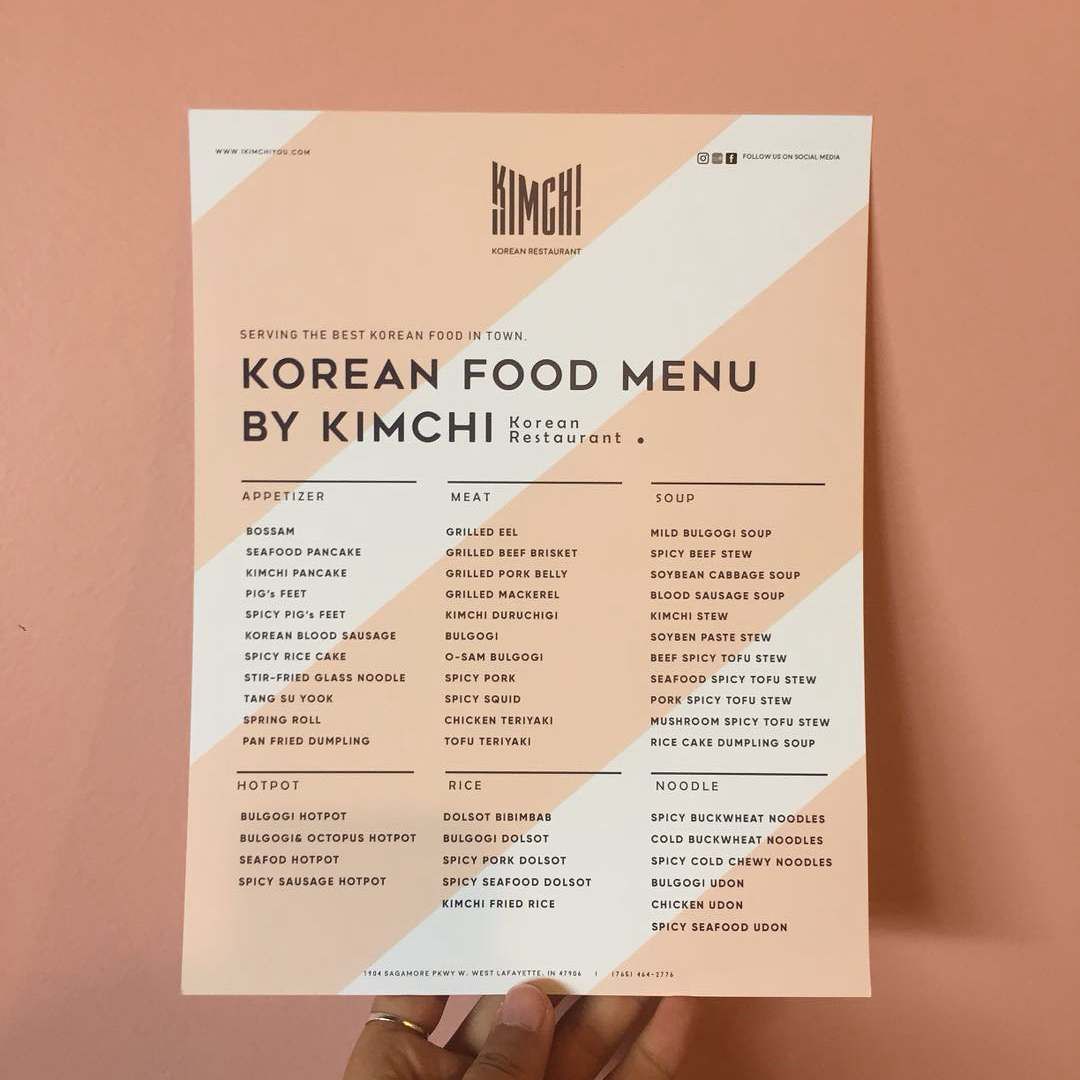 A person is holding a korean food menu by kimchi