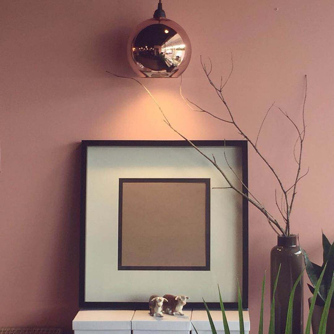 A picture frame is hanging on a pink wall next to a vase of plants
