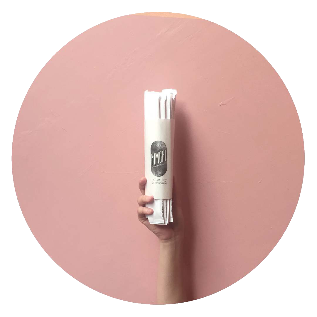 A hand is holding a newspaper in front of a pink wall.