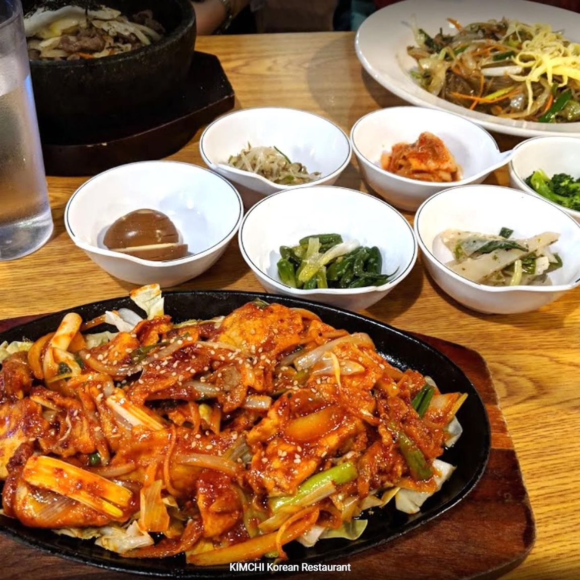 A sizzling plate of food is surrounded by bowls of food on a wooden table.