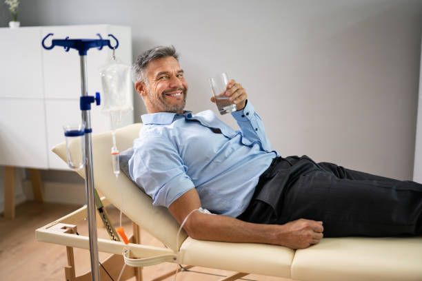 A man is laying in a bed holding a glass of water.