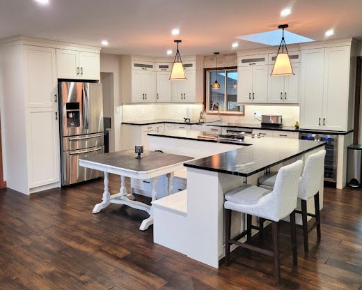 A modern kitchen with white cabinets, a dark island with integrated seating, stainless steel appliances, and wood floors.