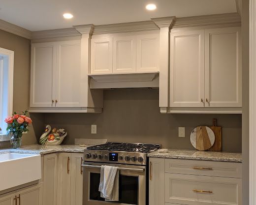 A kitchen area featuring light beige cabinets, a farmhouse sink, stainless steel stove, and marble-style countertops.