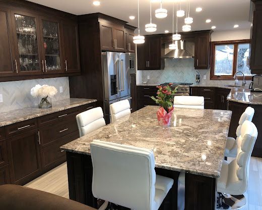 Modern kitchen featuring dark wood cabinets, a large granite island with white chairs, and hanging pendant lights.