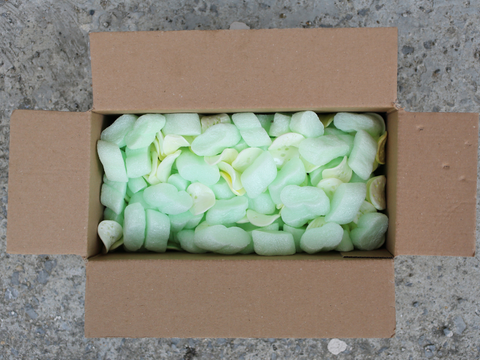 A cardboard box filled with green packing peanuts