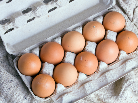 A cardboard box filled with brown eggs on a table.