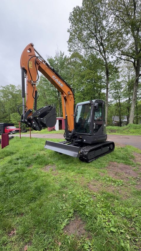 Orange and black Case excavator on a grassy hill with trees in the background.