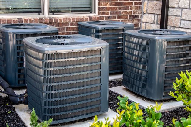 A row of air conditioners are sitting in front of a brick building.