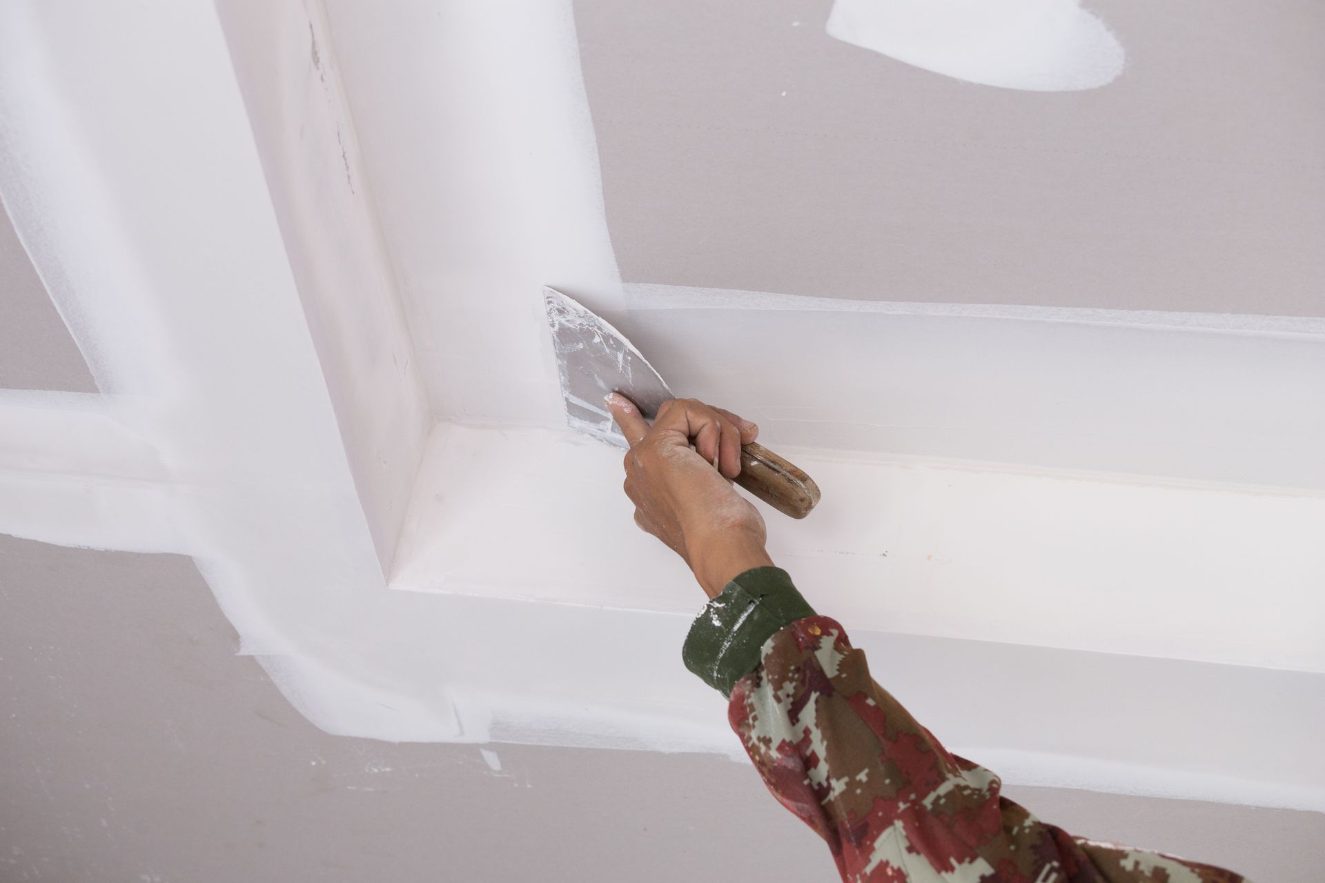 Close-up of a worker's hand carefully applying gypsum plaster to ceiling joints, creating a smooth and seamless finish.