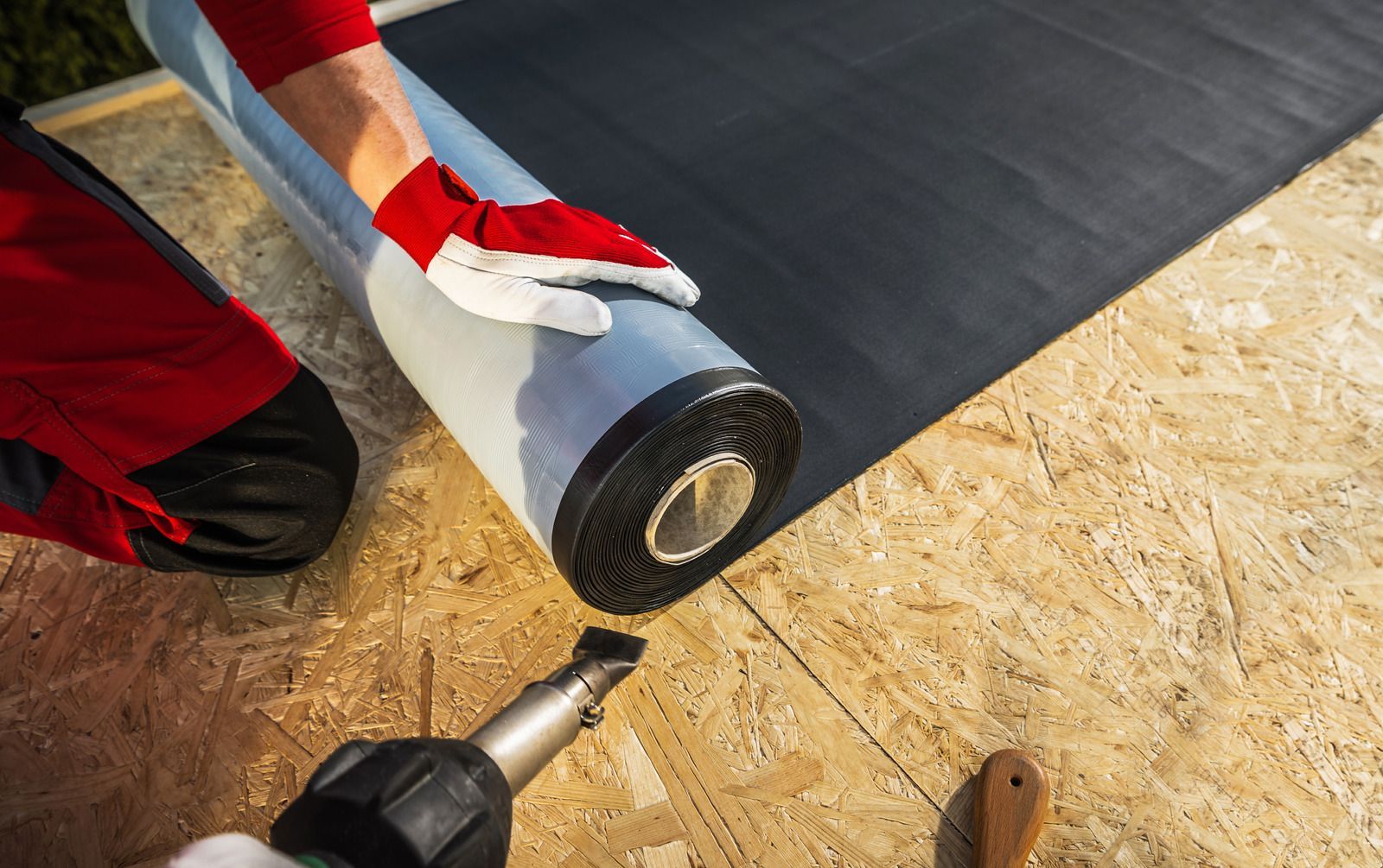 A person is laying a roll of roofing material on a roof.