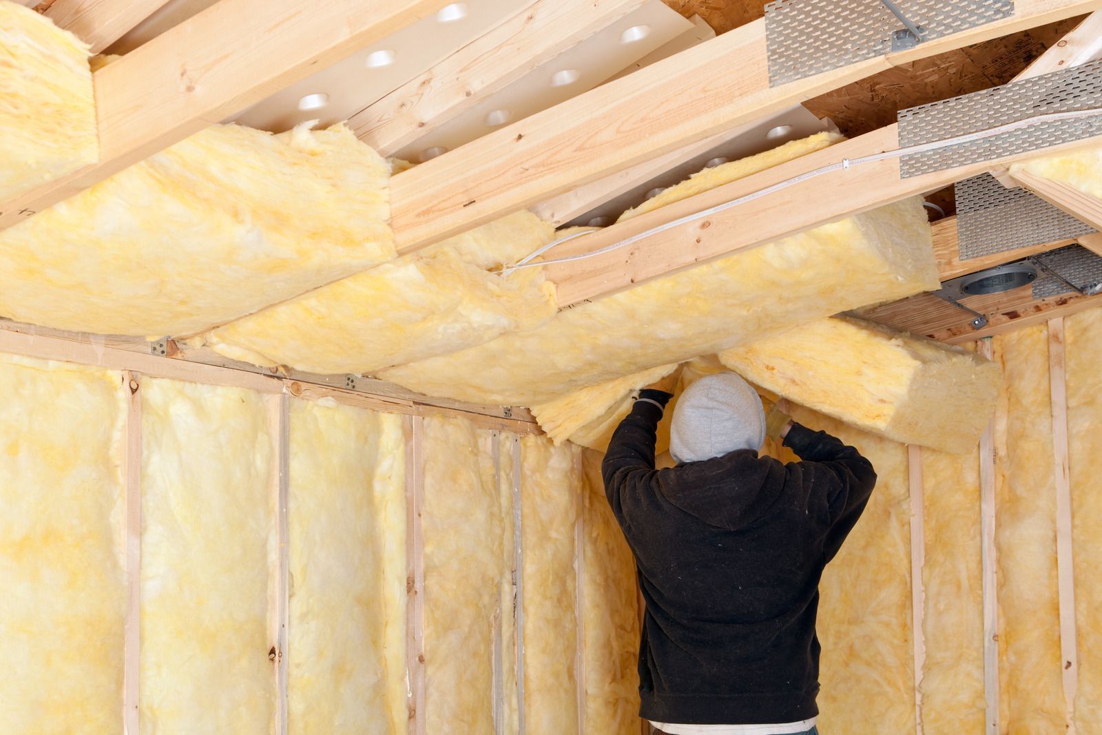 A man is installing insulation on the ceiling of a building.