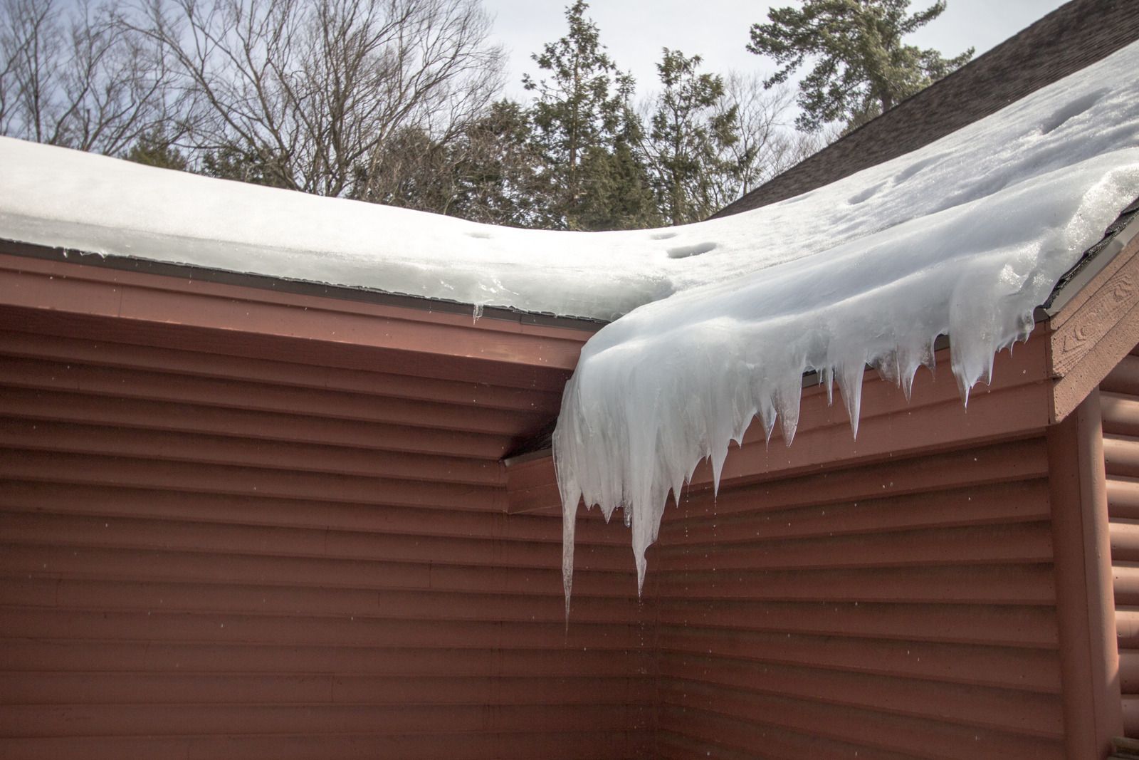 Icicles are hanging from the roof of a log cabin.