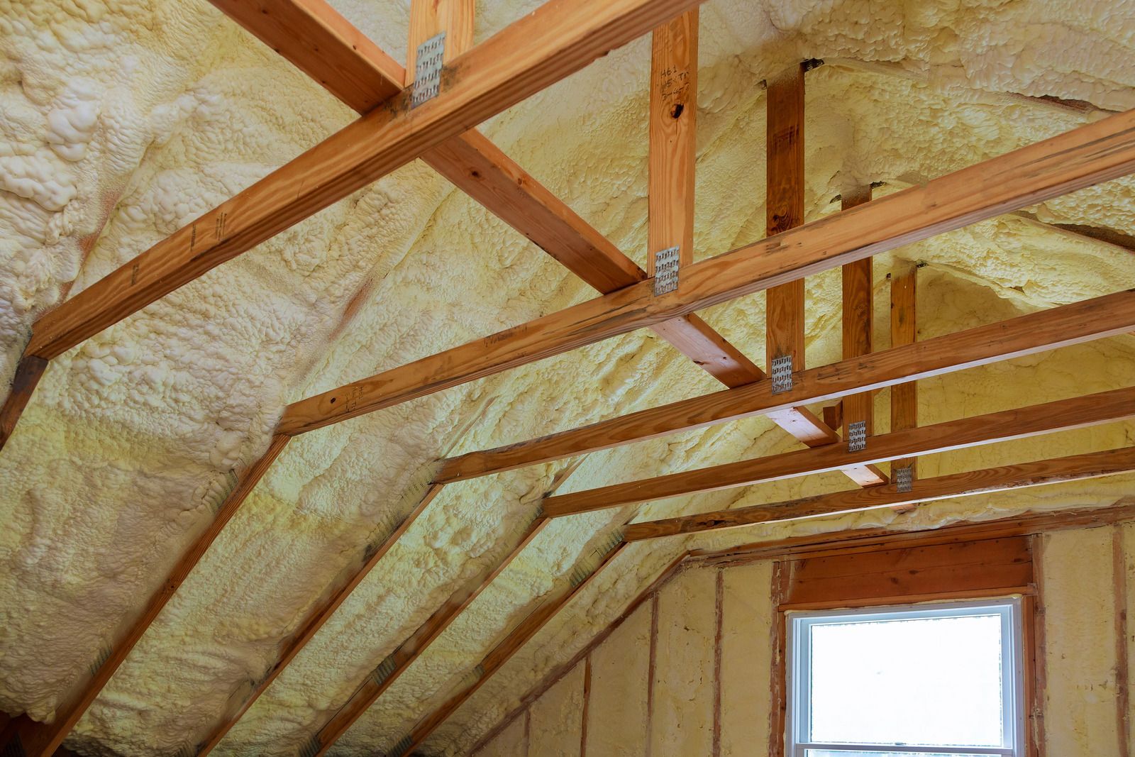 The ceiling of a house with wooden beams and foam insulation.