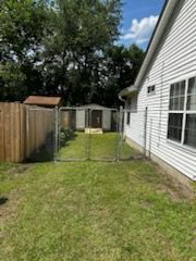 A backyard with a wooden fence, chain-link fence, and a white house. A small shed is visible inside the chain-link fence.