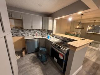 A kitchen with gray cabinets, appliances, and countertops. A bar counter separates the kitchen from a living area.