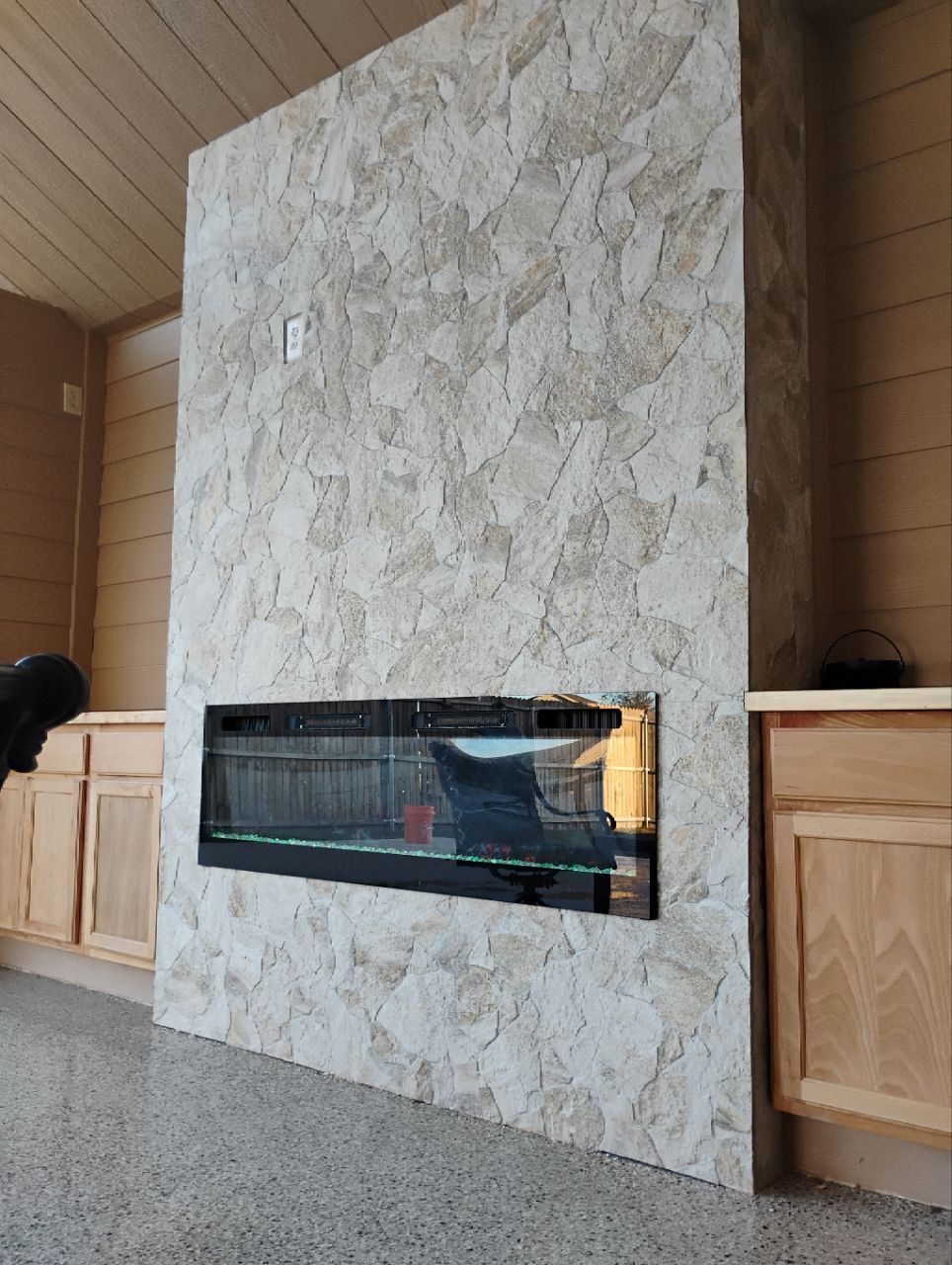 Fireplace with dark glass, mounted in a wall covered in textured panels, built into a wood-paneled room.