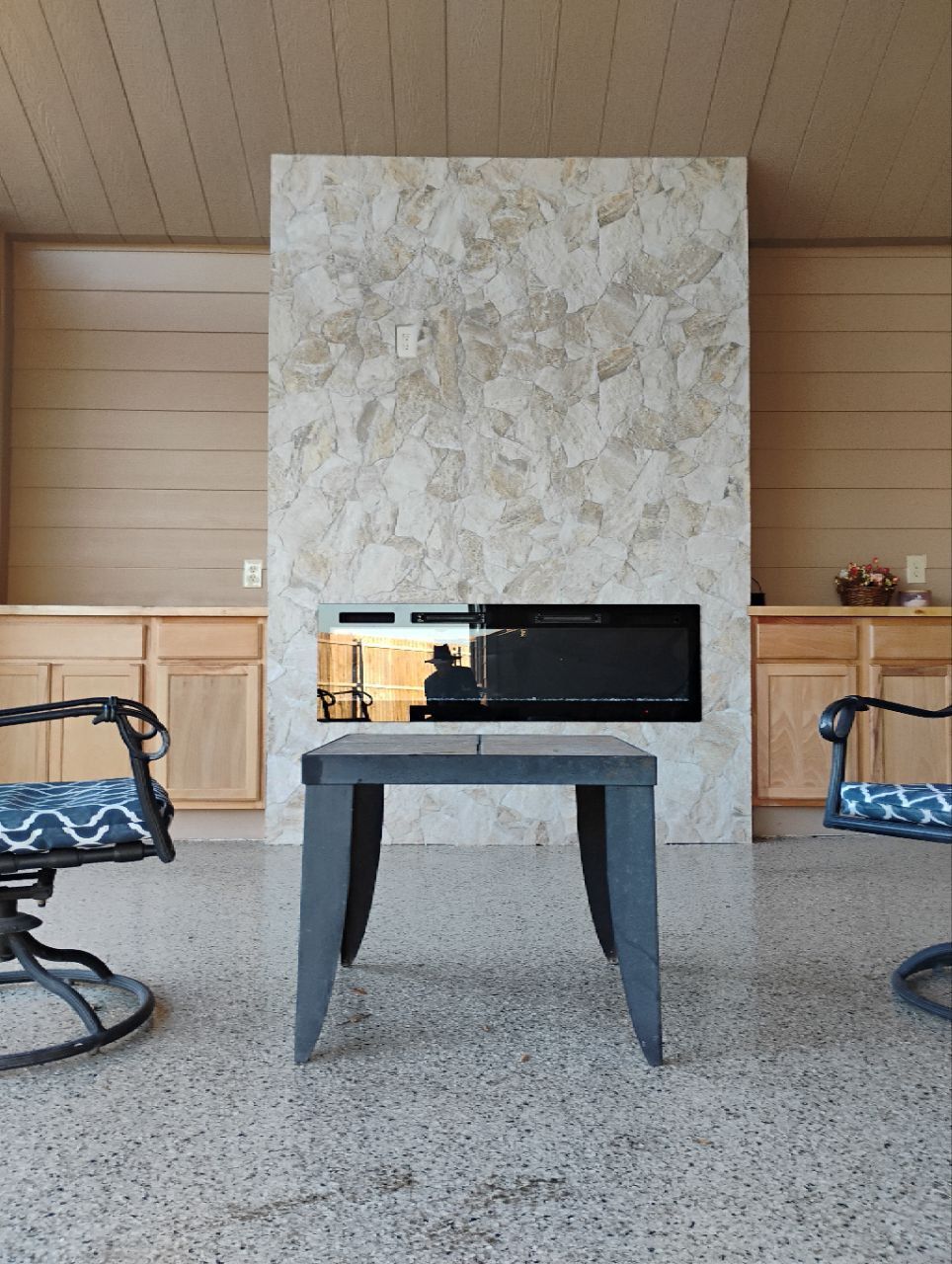 A modern outdoor space with a fireplace. A table sits in front of the fireplace, with chairs on either side.