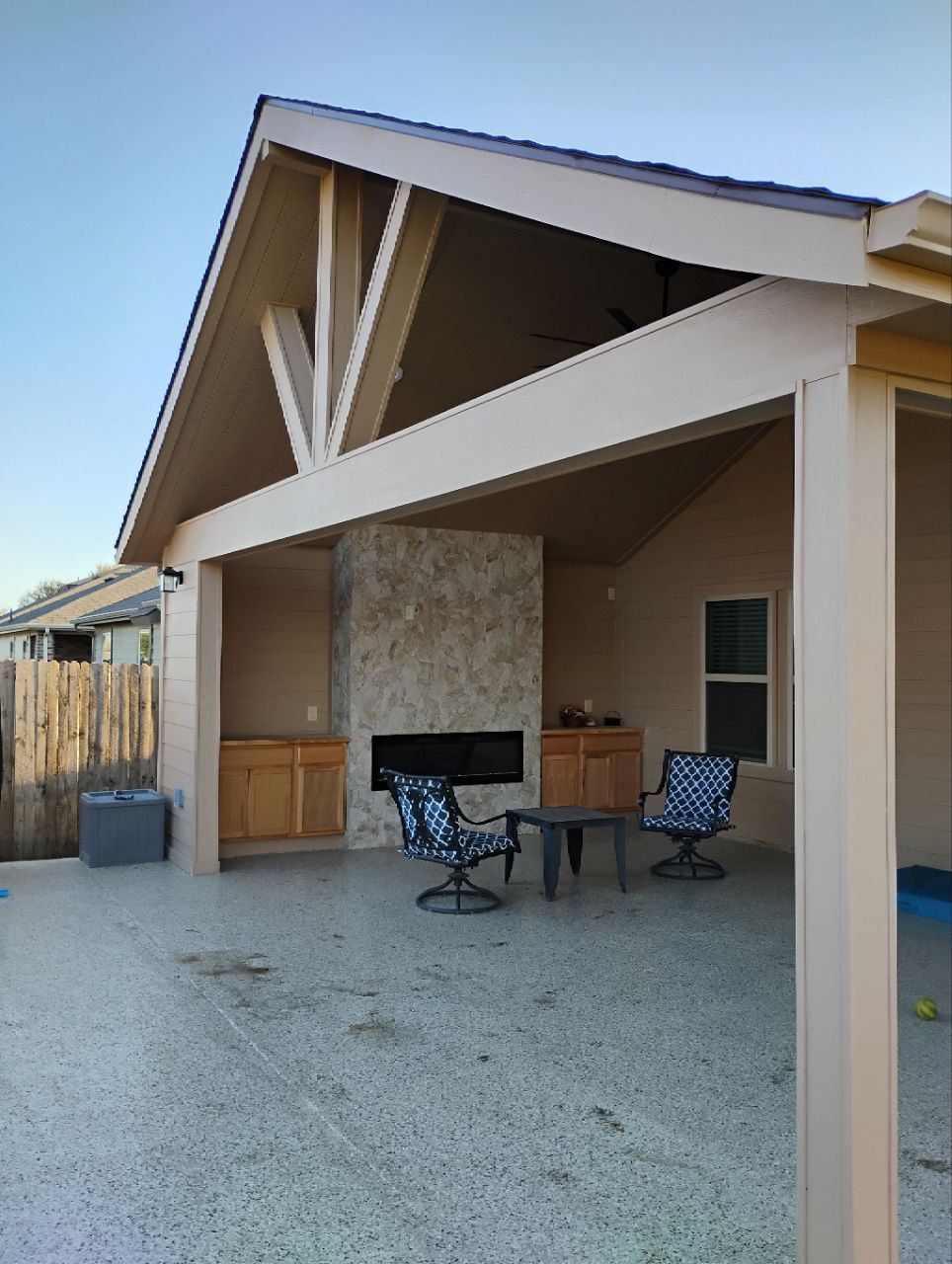 Covered patio with a fireplace and seating. Beige exterior, concrete floor, blue sky.