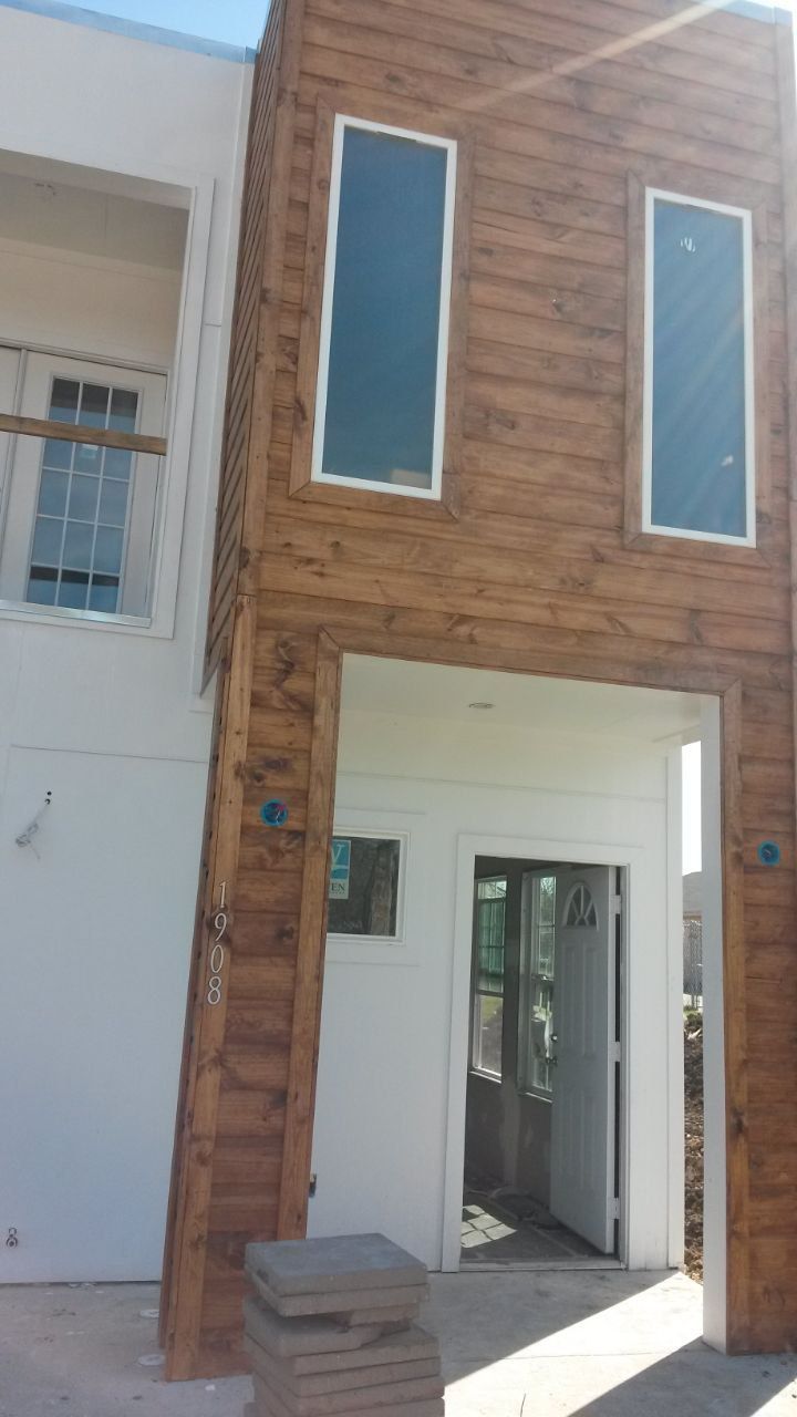 Exterior of two-story building. Brown wood-look siding, tall windows, white entrance with open door, and white building section.